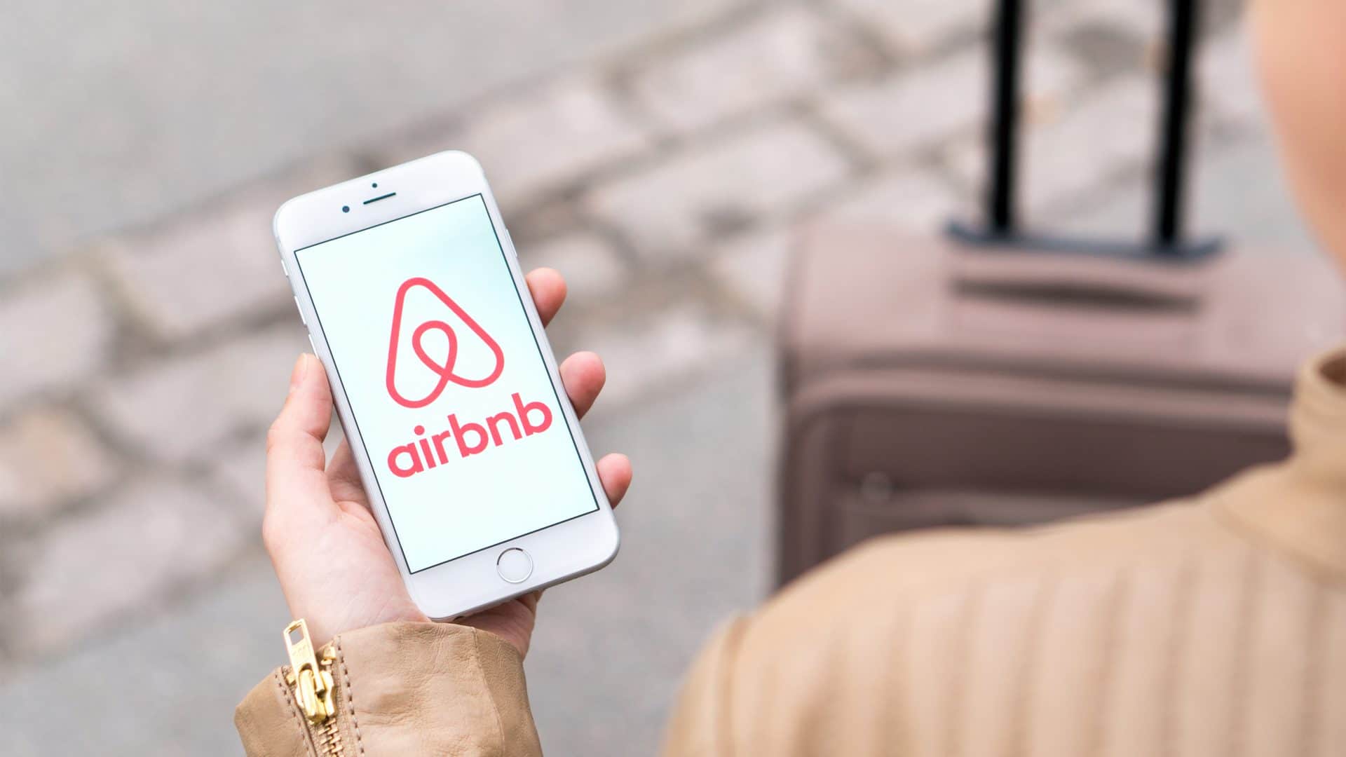 Mão branca segurando celular com logo do airbnb