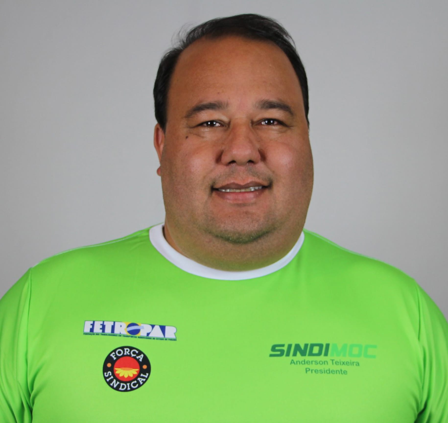 homem pardo, obeso, de camiseta verde, sorrindo.