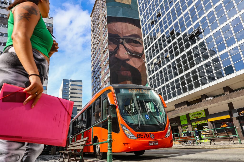 mulher em primeiro plano e ônibus biarticulado passando