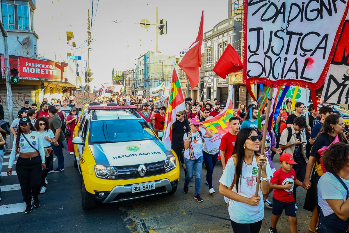 pessoas protestando no centro e uma viatura da PM ao meio