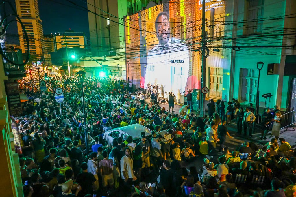 Image of actor Lázaro Ramos commenting on the Oscars projected on the facade of Cine Passeio and a crowd watching the broadcast