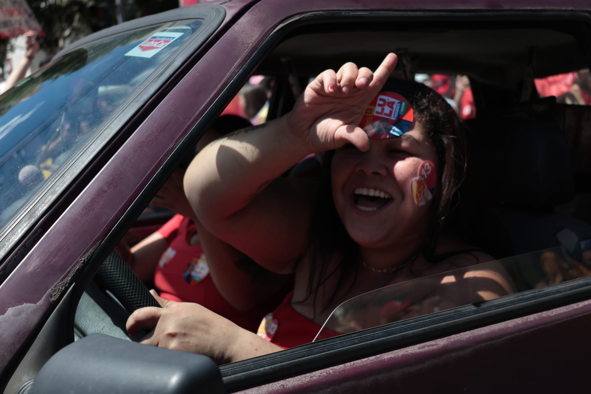mulher branca, dirigindo, fazendo gesto de L com as mãos, sorrindo