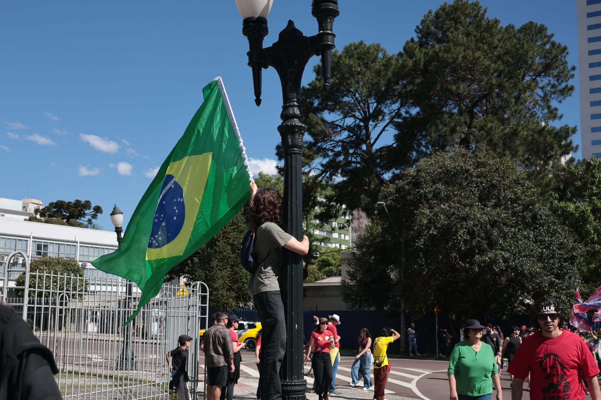 homem branco segurando em poste com a bandeira do Brasil