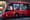 Ônibus vermelho do transporte coletivo de Curitiba, com o logotipo da URBS e a inscrição 'cidade de curitiba', com passageiros atrás das janelas no fim de tarde.